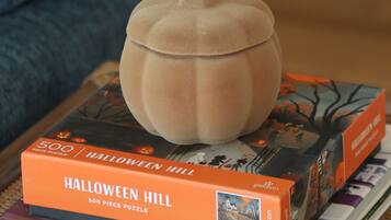 A pumpkin-shaped object on top of a book titled 'HALLOWEEN HILL' with a 500-piece puzzle.