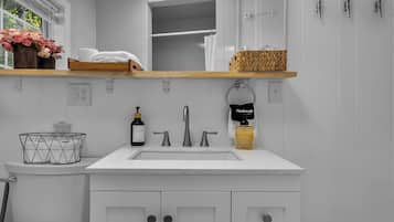 A bathroom with a white vanity, a mirror, a sink, and a shower. There are three lights above the mirror, and a basket of towels is visible.