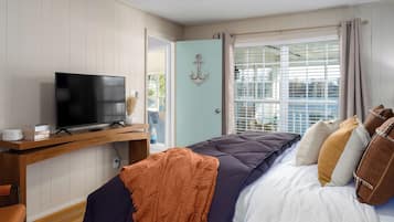 A bedroom with a bed, a television on a wooden stand, a window with curtains, and a door with an anchor decoration.
