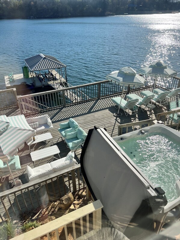 A deck with lounge chairs, a hot tub, and a view of a lake.