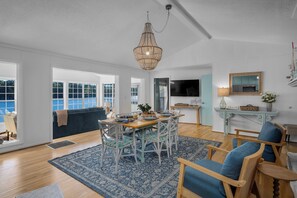 A spacious living area with a dining table, chairs, a chandelier, and a large window.