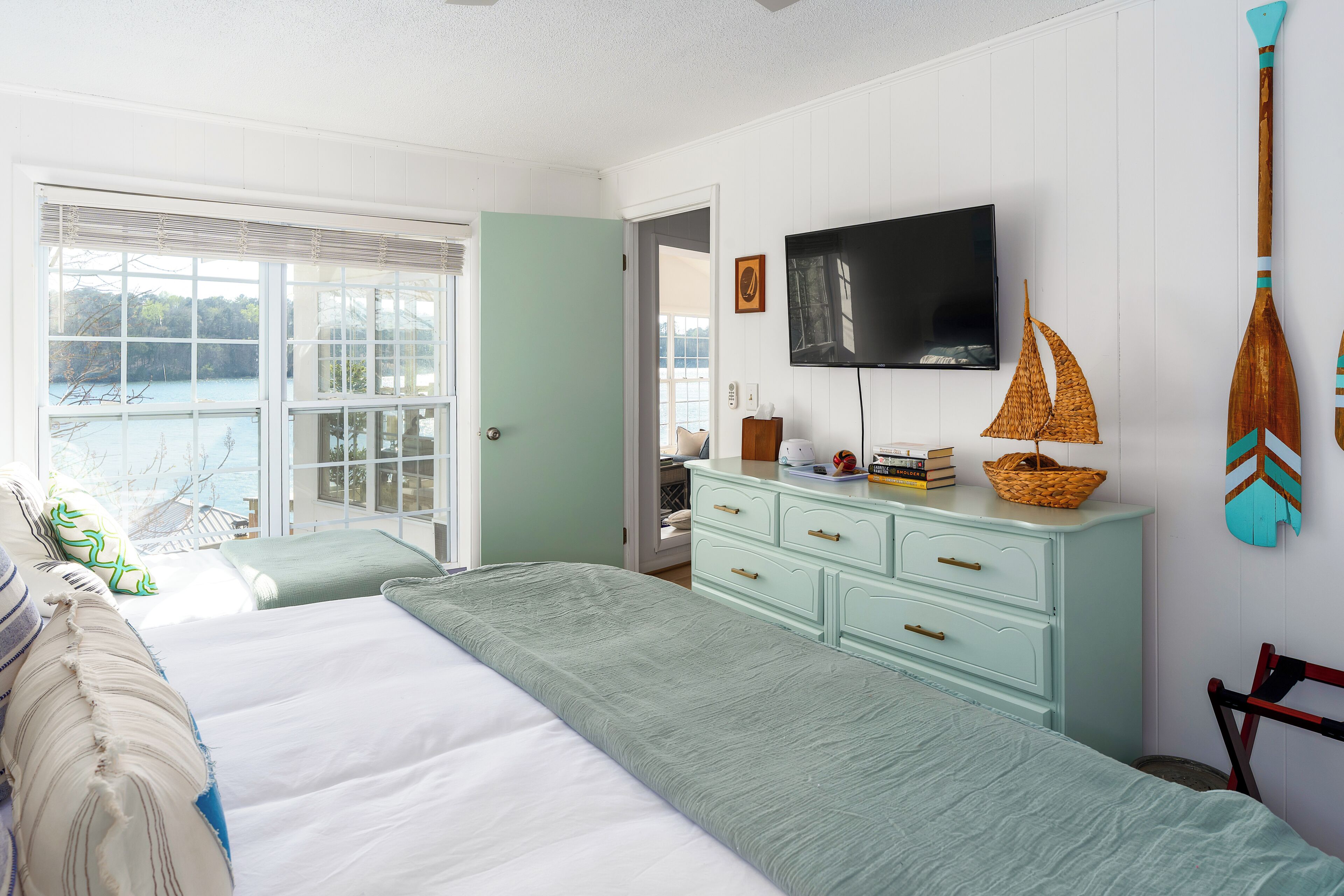 A bedroom with a large bed, a television, a dresser, and a view of the outdoors.