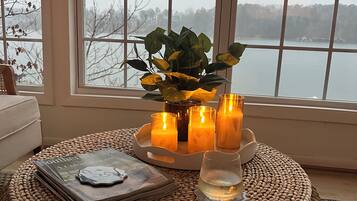 A cozy room with a large window, a woven ottoman, a tray with candles, and a magazine.