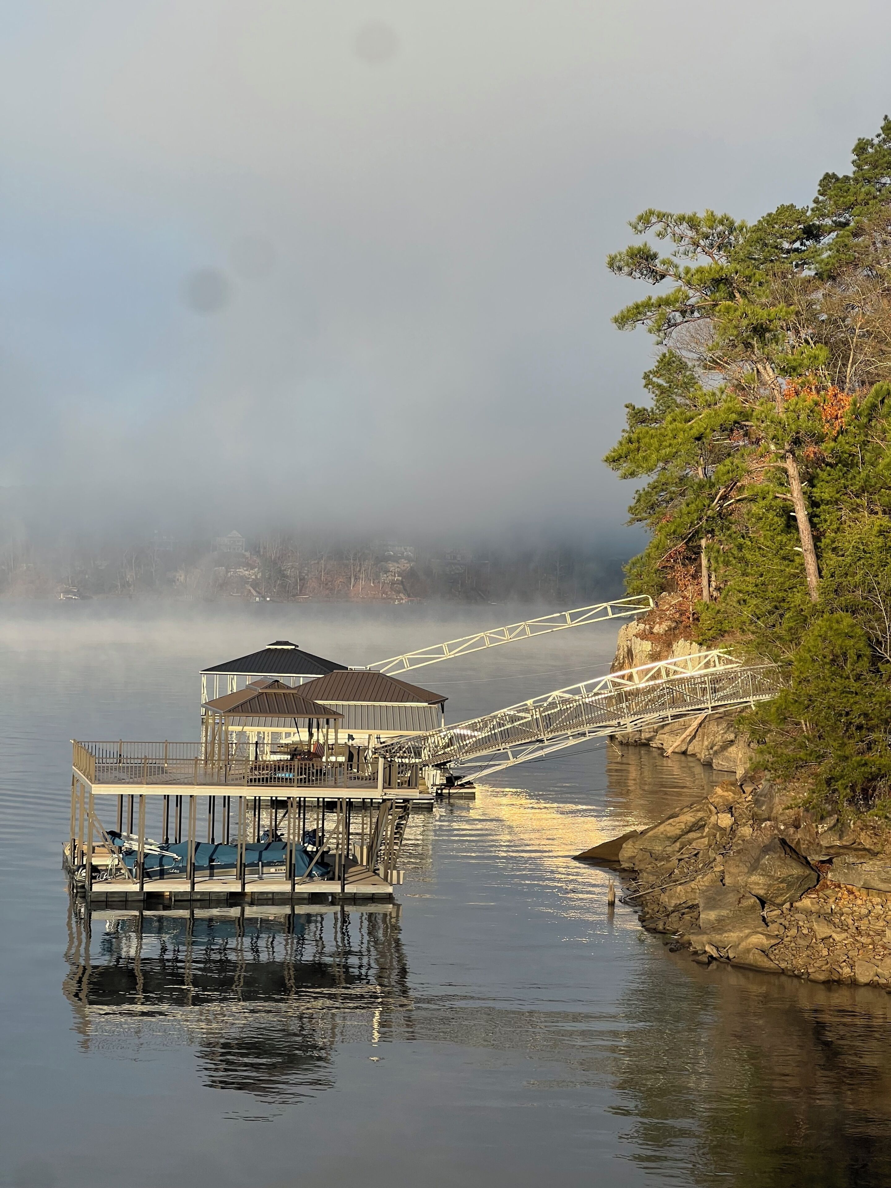 A pier extending into calm water with a gazebo-like structure and a bridge.