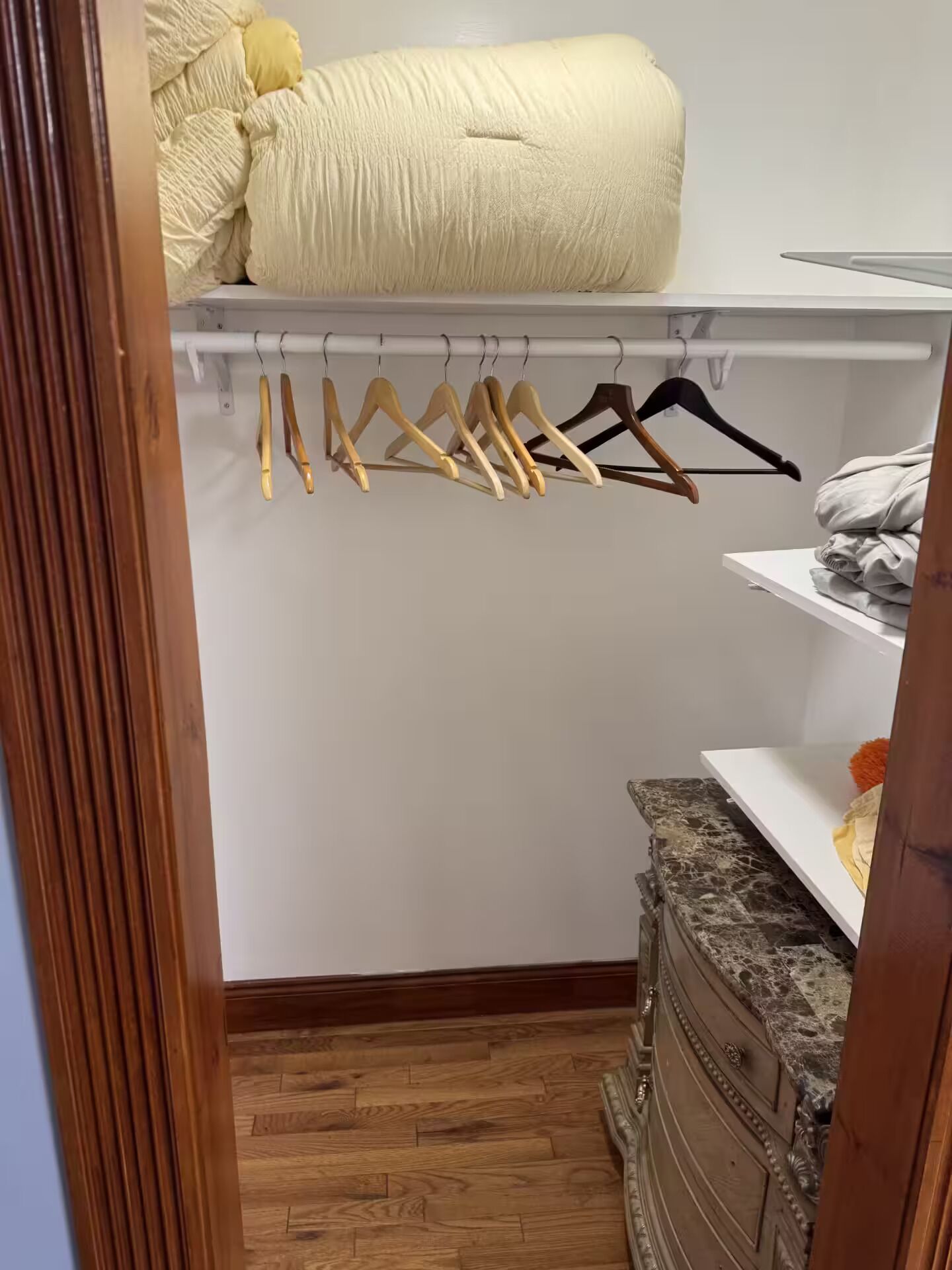 Un armario con perchas de madera, una cama y un tocador de mármol.