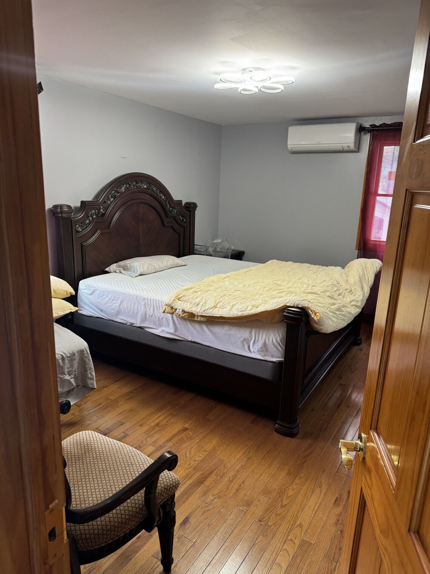 A bedroom with a wooden bed, a chair, and an air conditioning unit on the wall.