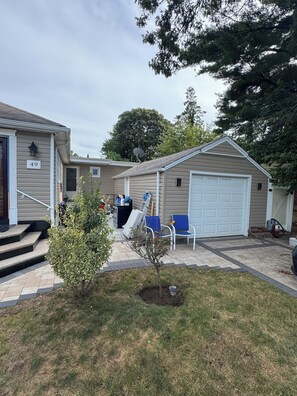 A residential property with a garage, a small patio area, and a front yard with a tree and steps leading to the entrance. - 4-bedroom Entire home in Valley Stream NY, 10 Min to JFK Near Shopping & NYC (Valley Stream)