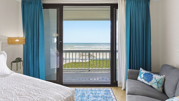 Ett hotellrum med en balkong, en säng, en soffa och utsikt över havet.