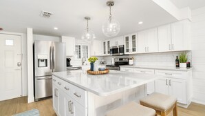 Una cocina moderna con armarios blancos, electrodomésticos de acero inoxidable y una isla central con taburetes.
