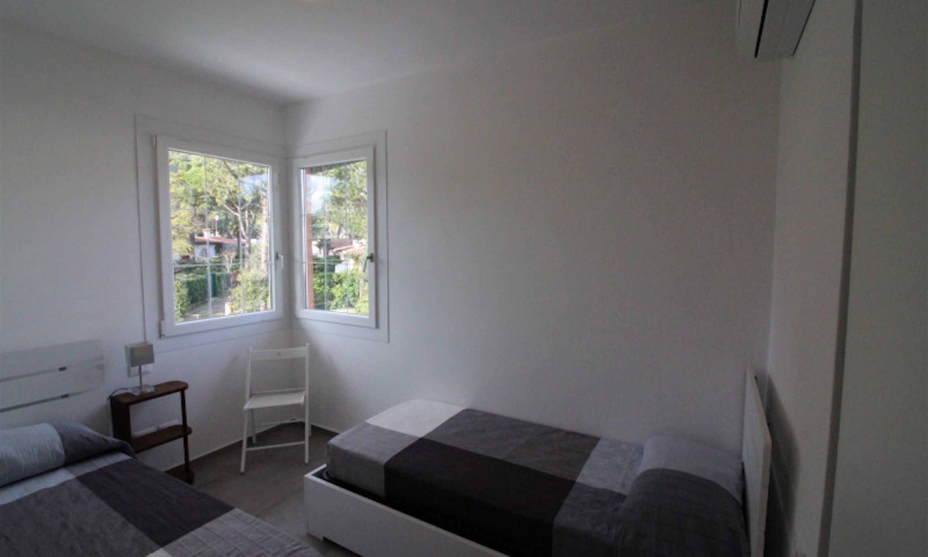 A bedroom with two beds, a chair, and a window with a view of greenery.