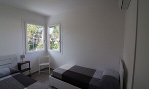 Slaapkamer met twee bedden, een stoel en een raam met uitzicht op groen.