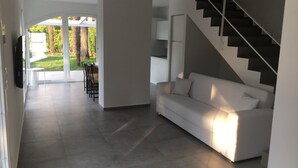 A modern interior with a white sofa, a staircase, and a view of a garden through glass doors. - Modern Villa a few Steps From the Beach (Lignano Sabbiadoro)