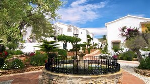 A courtyard with a fountain, stone pathway, and white buildings with arched windows. - Holiday Home 'Los Naranjos' with Shared Pool, Wi-Fi and Air Conditioning (Nerja)