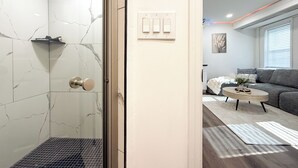 Een moderne badkamer met een glazen douchedeur, een marmeren wand en een zichtbare lichtschakelaar.