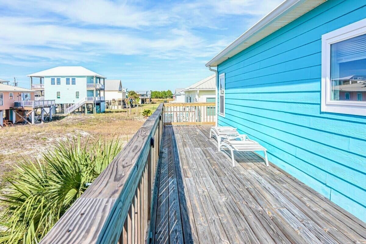 A wooden deck with a railing, a blue building, and a white building in the background.