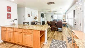 Een ruime keuken met een groot eiland, houten keukenkastjes en een eethoek met stoelen en een tafel.
