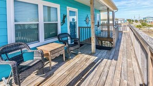 Een houten terras met een tafel en stoelen, een overdekte veranda en een blauw huis met witte details.