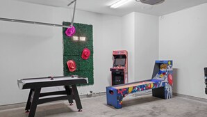 Una mesa de billar, una máquina de pinball y un letrero de neón en una habitación con paredes blancas y suelo de hormigón.