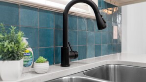 Una cocina con grifo negro, pileta de acero inoxidable y salpicadero de azulejos.
