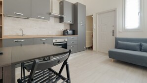 Ett modernt kök med grå skåp, ett matbord med stolar, en inbyggd ugn och en blå soffa i det intilliggande vardagsrummet.