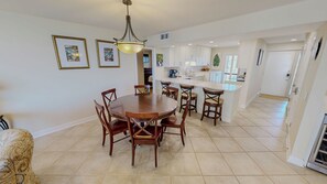 A dining area with a round table and chairs, a kitchen with white cabinets, and a hallway leading to a door. - Recently Remodeled Mainsail 136 Stunning Beach Facing (Miramar Beach)