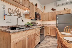 A kitchen with wooden cabinets, a granite countertop, stainless steel appliances, and a dining area with a wooden table and chairs. - Newly Built 3BD 2BTH| Kid+Pet Friendly|Sleeps 7 (Spirit Lake)
