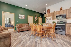 A room with a dining table, chairs, a sofa, and a kitchen area with cabinets and appliances. - Newly Built 3BD 2BTH| Kid+Pet Friendly|Sleeps 7 (Spirit Lake)