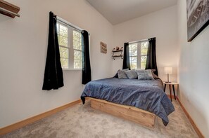 A bedroom with a bed, two windows, a nightstand, a lamp, and a wall-mounted shelf. - Newly Built 3BD 2BTH| Kid+Pet Friendly|Sleeps 7 (Spirit Lake)