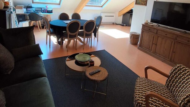 A loft-style living room with a dining area, wooden beams, a TV, and a large window. - 4p apartment in village center (Laruns)