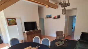 A dining area with a round table, chairs, a television, and a sofa. - 4p apartment in village center (Laruns)