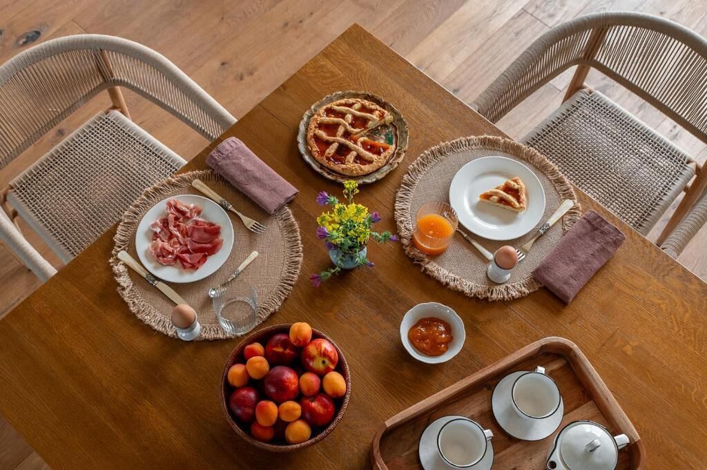 A wooden dining table with a pie, plates of food, a bowl of fruit, and teapots.