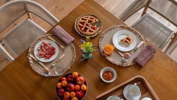 A wooden dining table with a pie, plates of food, a bowl of fruit, and teapots.