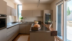 Une cuisine moderne dotée d’un îlot central, d’appareils électroménagers en acier inoxydable et d’une grande fenêtre offrant une vue sur l’extérieur.