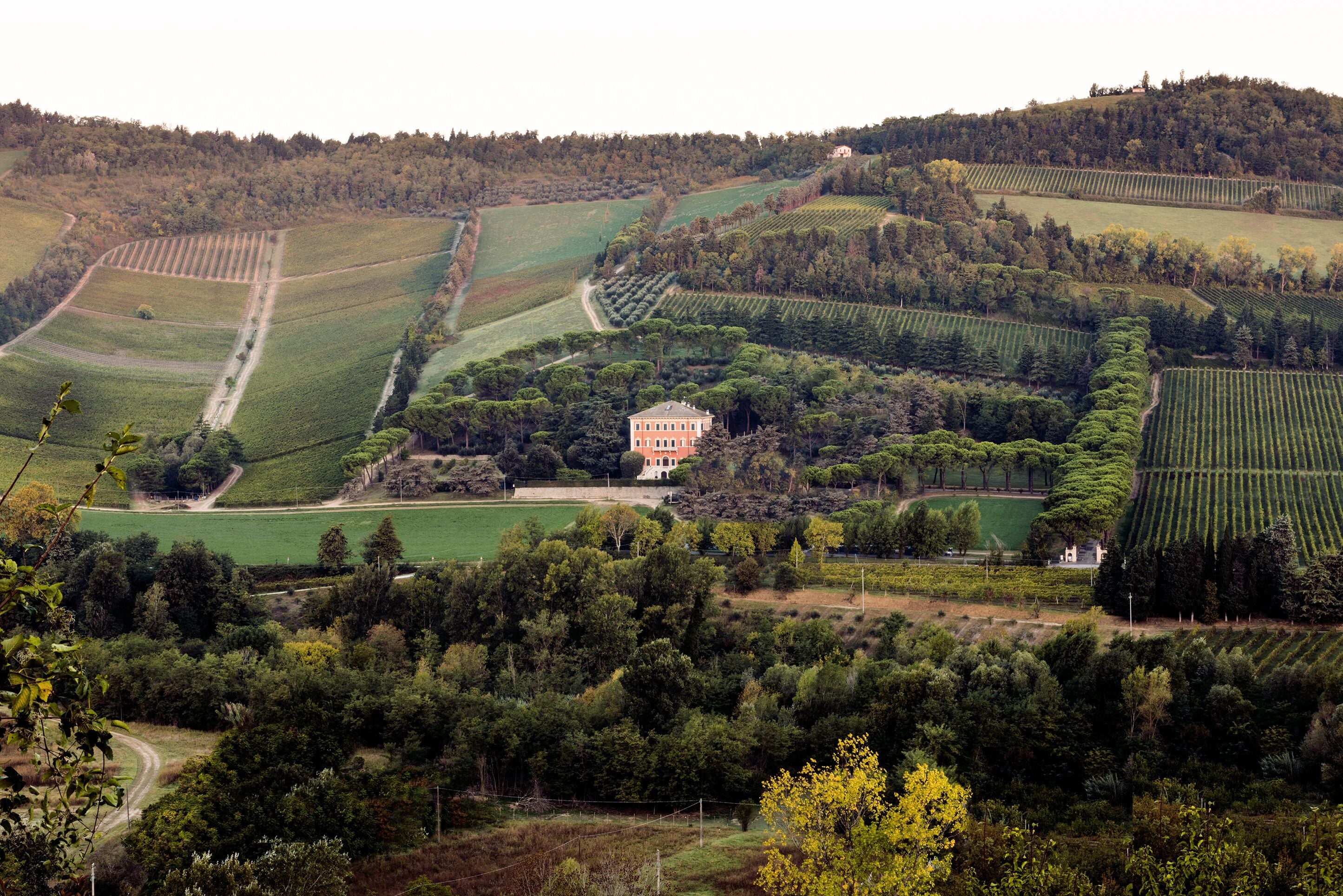 Un vaste domaine comprenant de grandes étendues de champs, un bâtiment principal et de denses forêts environnantes.