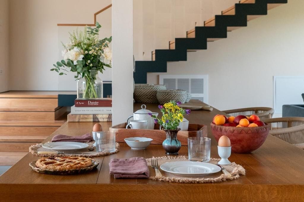 A dining table set with plates, glasses, and a bowl of fruit.