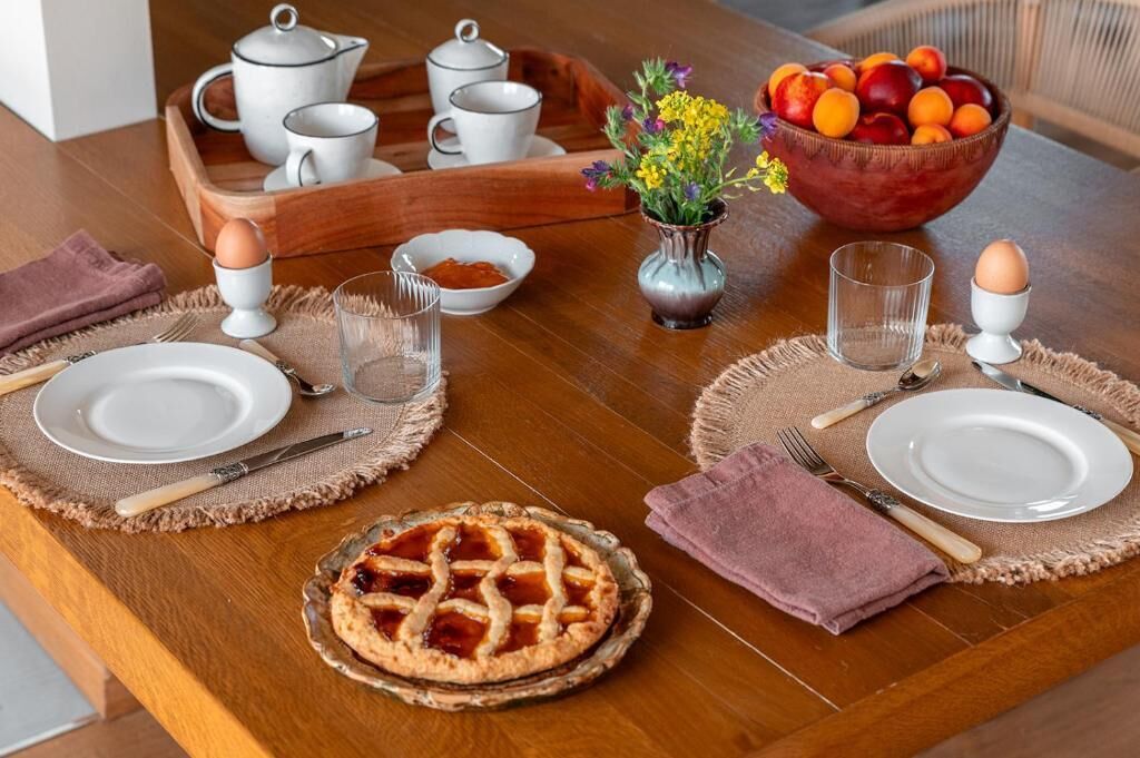 A dining table set with plates, cutlery, glasses, a pie, a fruit bowl, and a vase with flowers.