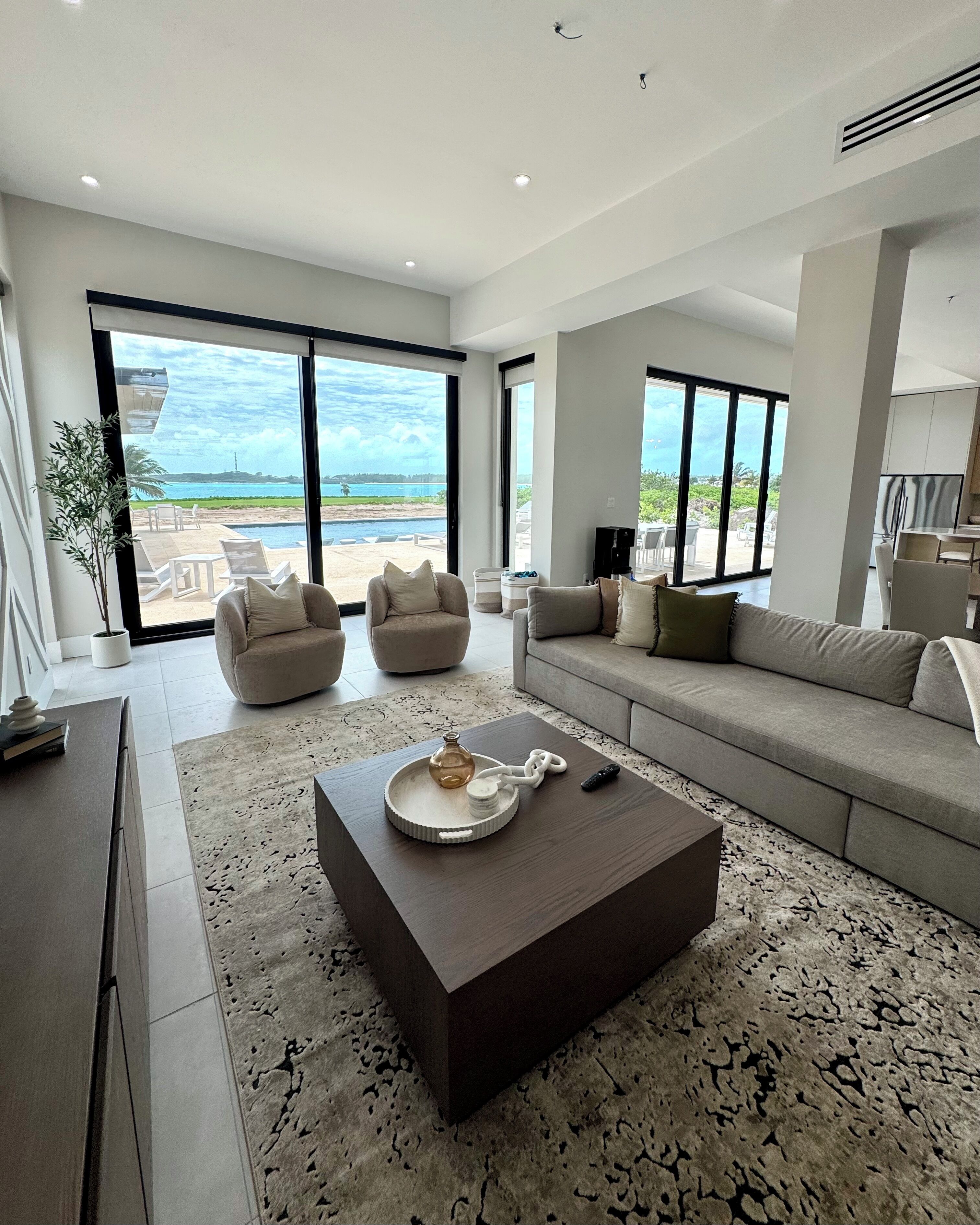 A spacious living room with a large sofa, two armchairs, a coffee table, and a view of the ocean.