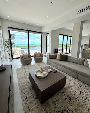 A spacious living room with a large sofa, two armchairs, a coffee table, and a view of the ocean. - Seaside Villa - Brand New Modern Luxury 7 Bedrooms + 9 Bathrooms + Concierge (Exuma)
