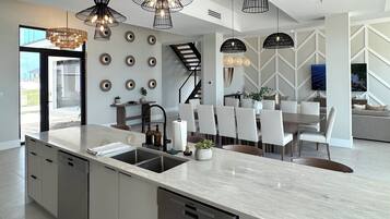 A modern kitchen with a large island, pendant lighting, and a dining area with chairs.