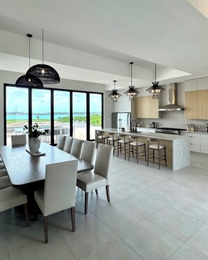 A modern kitchen with large windows, a dining area with a view, and a bar area. - Seaside Villa - Brand New Modern Luxury 7 Bedrooms + 9 Bathrooms + Concierge (Exuma)