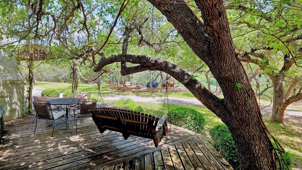 Eine Holzdielen-Terrasse mit einer Bank und einem Tisch, umgeben von Bäumen und einer Rasenfläche.