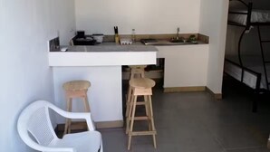 Cocina compacta con un taburete de bar, una mesa pequeña y una cama litera al fondo.