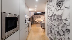 A modern kitchen with a built-in microwave, a dining area with a table and chairs, and a wall with a floral mural. - Ribeira Spacious Apartment for 6 (Oporto)