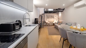 A modern kitchen with a built-in toaster, a sink, and a stove. There is a dining area with a glass table and chairs, and a sofa in the background. - Ribeira Spacious Apartment for 6 (Oporto)
