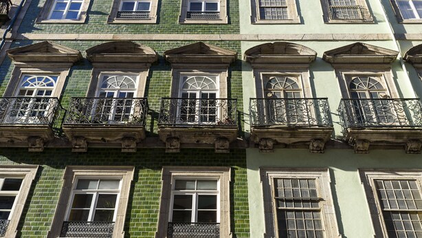 A multi-story building with a green facade, multiple windows with white frames, and decorative iron balconies. - Ribeira Spacious Apartment for 6 (Oporto)