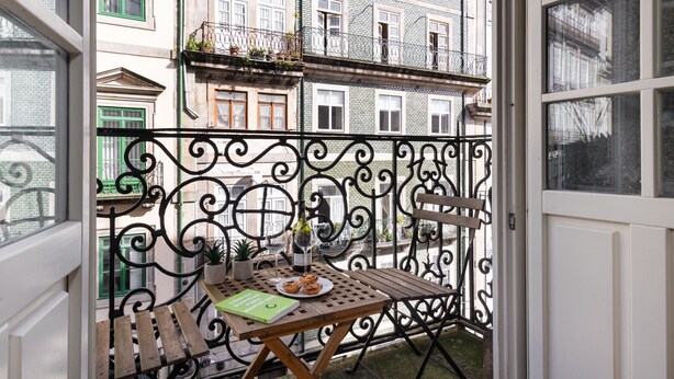 A balcony with a wooden table, a chair, a potted plant, and a bottle. - Ribeira Large Apt for 6 (Oporto)