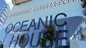 Un bâtiment moderne doté d’une façade en verre réfléchissant et sur lequel on peut lire en grand « OCEANIC HOUSE ».