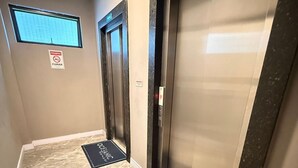 Un couloir avec deux ascenseurs, une fenêtre et un panneau indiquant « Il est interdit de fumer ».