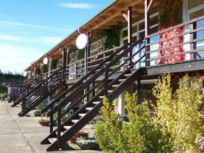 Una hilera de edificios de madera con escaleras exteriores, plantas en macetas y luces colgantes.