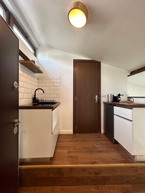 A compact kitchen with white cabinets, a wooden countertop, a black faucet, and a wooden door. - Cismigiu -Deluxe Apartment (Bucharest)